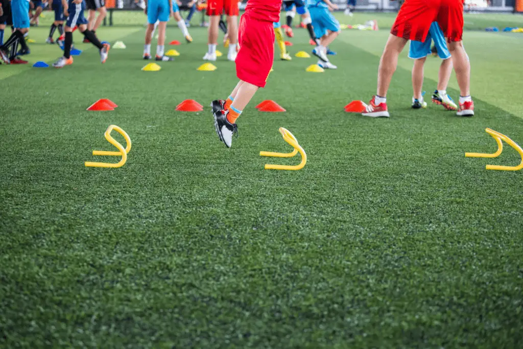 A person is jumping over a yellow agility ladder during physical soccer training.