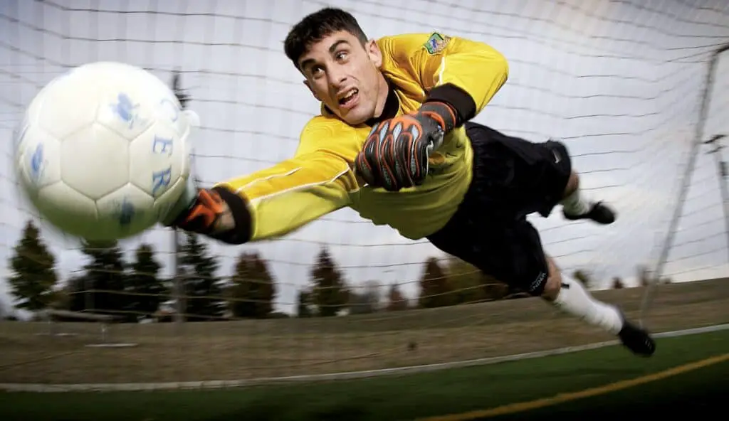 A goalkeeper wearing a yellow jersey making a save. Why do soccer goalies wear different uniforms?