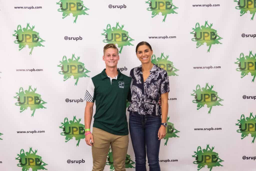 Sean Tinney standing next to Alex Morgan in front of a Slippery Rock University UPB backdrop.