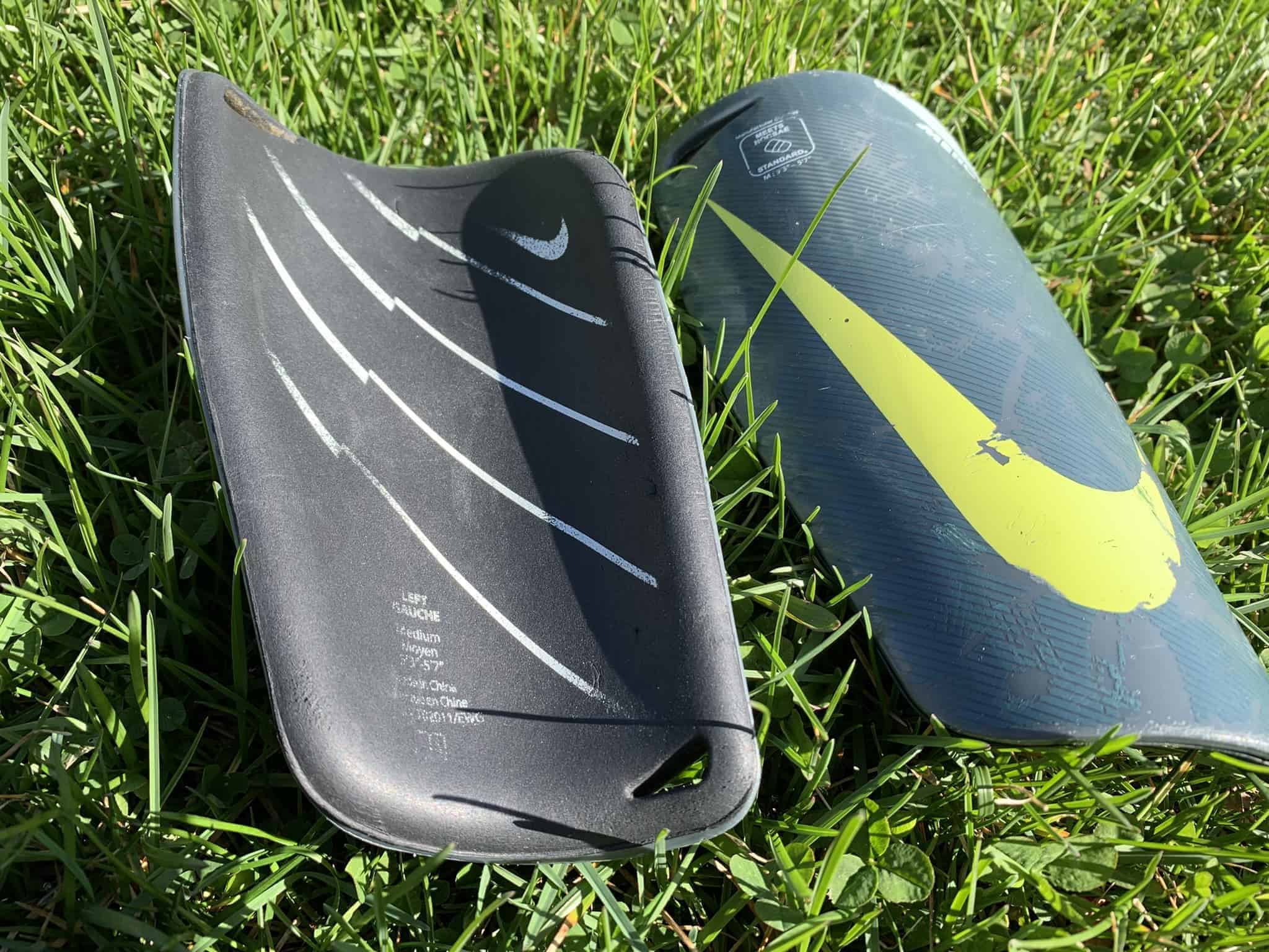 Two Nike soccer shin guards. One shows the inside and the other shows the outside with a yellow-green Nike swoosh symbol.
