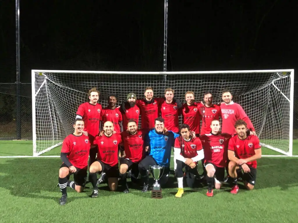 A soccer team wearing red jerseys poses in front of the 2022 Greater Pittsburgh Soccer League trophy after winning the championship in November.