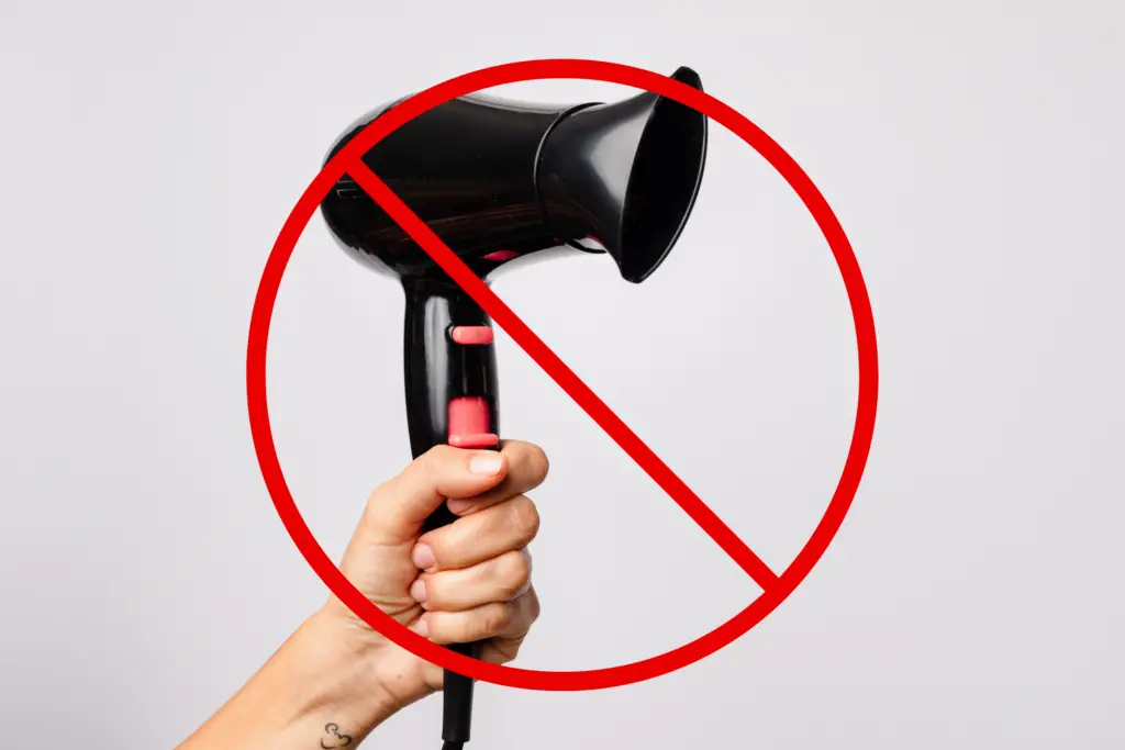 A person holds a hair dryer with a "prohibited" symbol overtop.