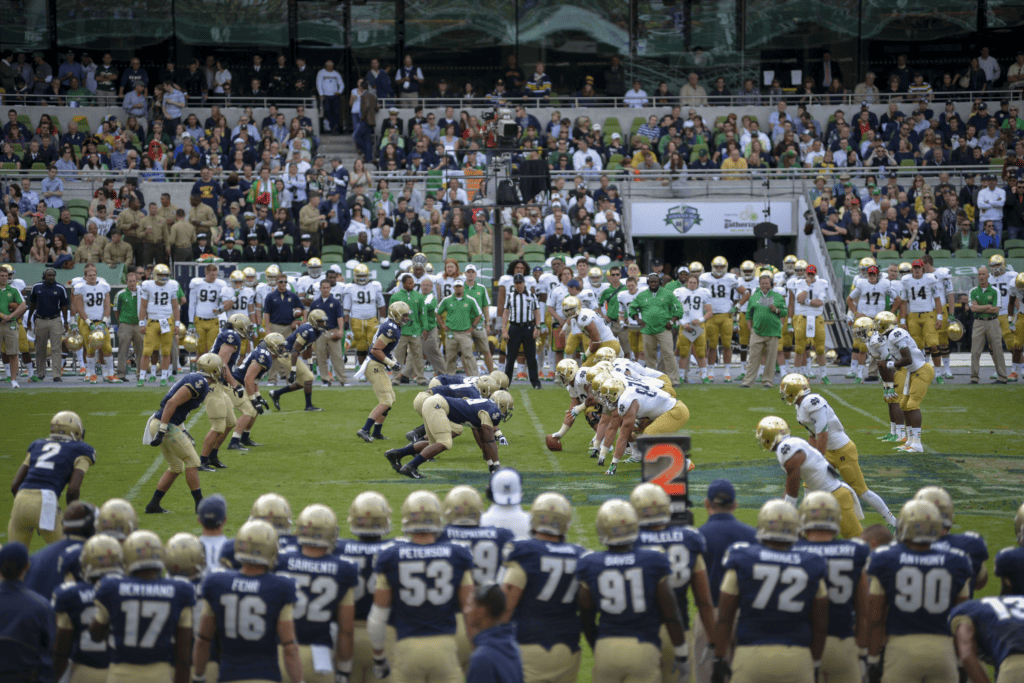 Two college football teams line up near the 45-yard line before a second down snap.
