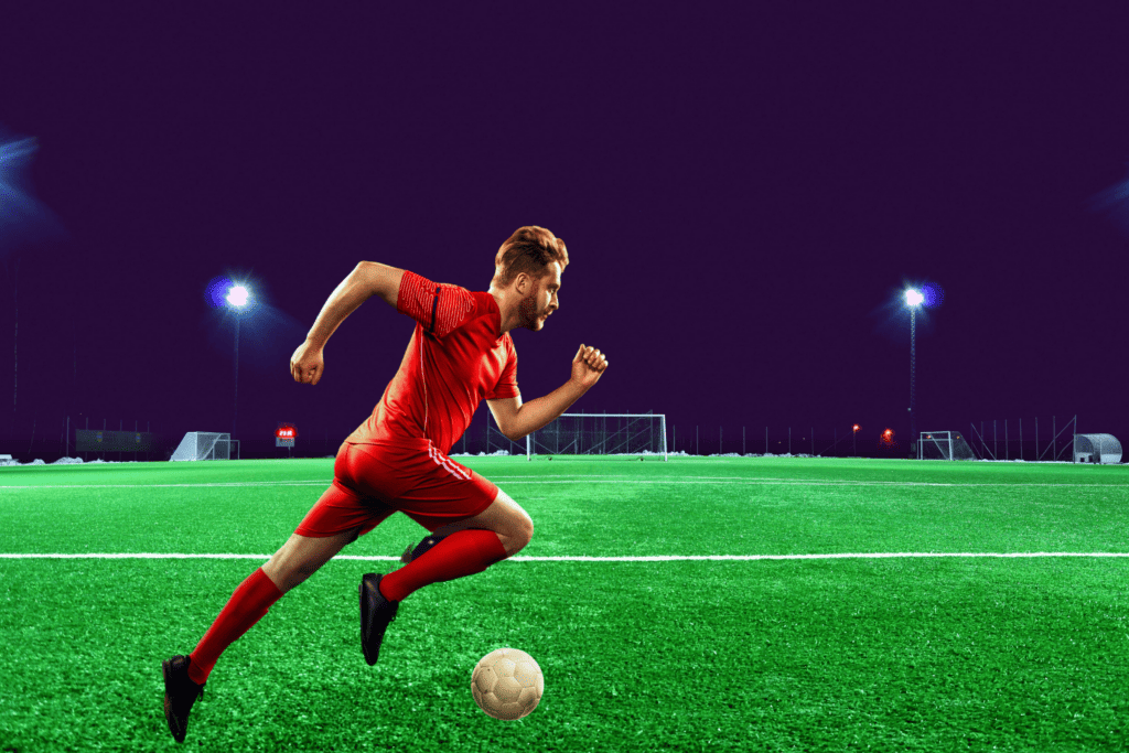 A graphic of a man dribbling a soccer ball on a turf field underneath shining floodlights.