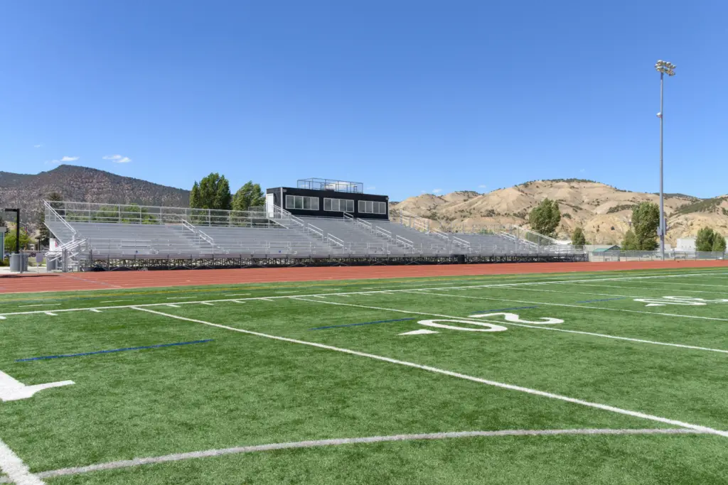 Bleachers overlook a high school track and turf field with mountains in the background.