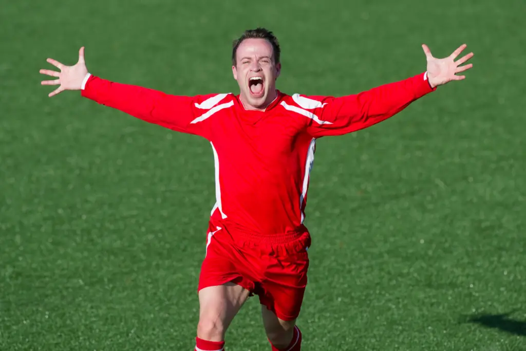 A college soccer player wearing red opens running with his mouth open and his arms wide.